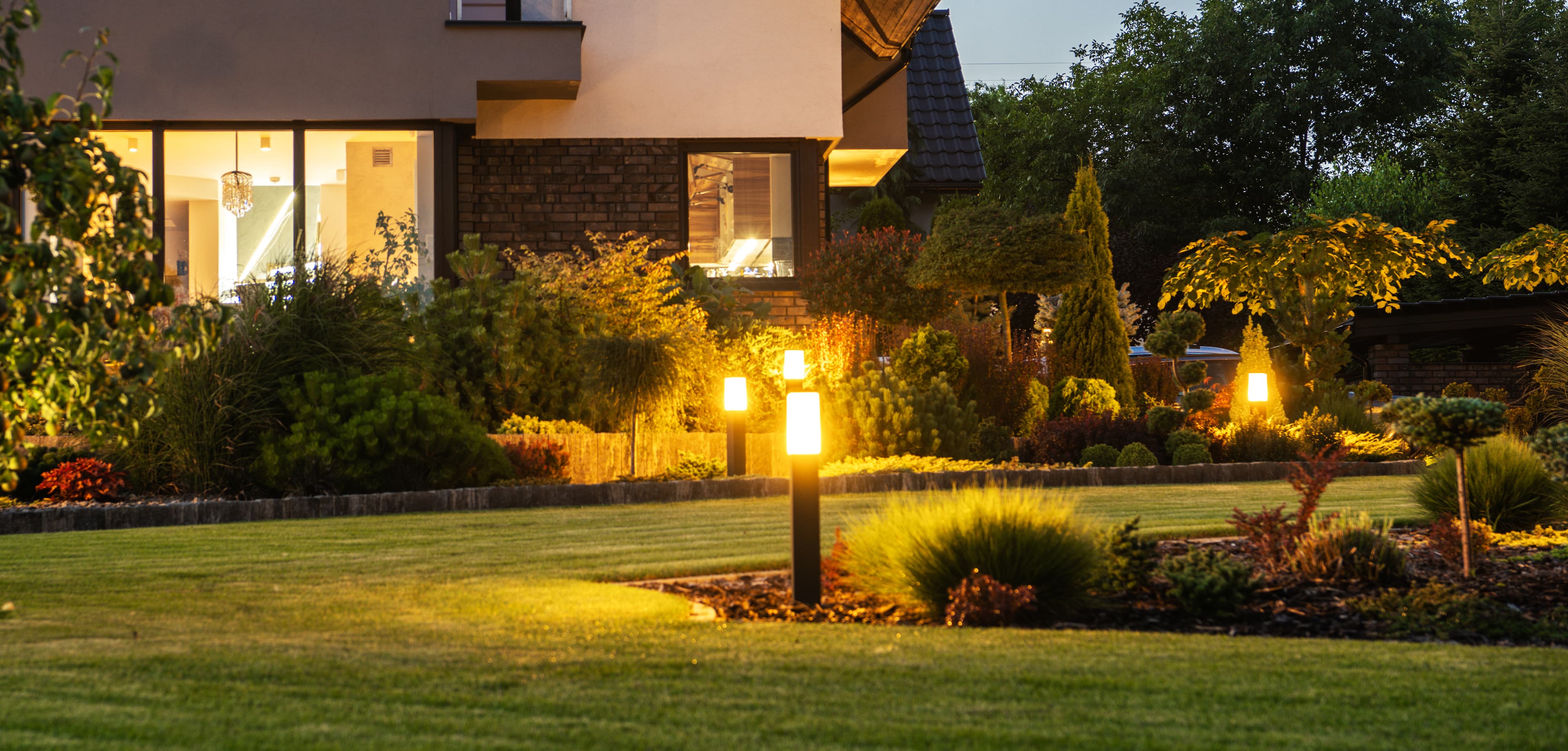 Landscape lighting fixtures illuminating a front yard at dusk
